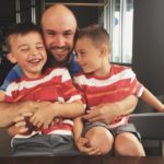 A smiling dad holds his laughing sons in his lap